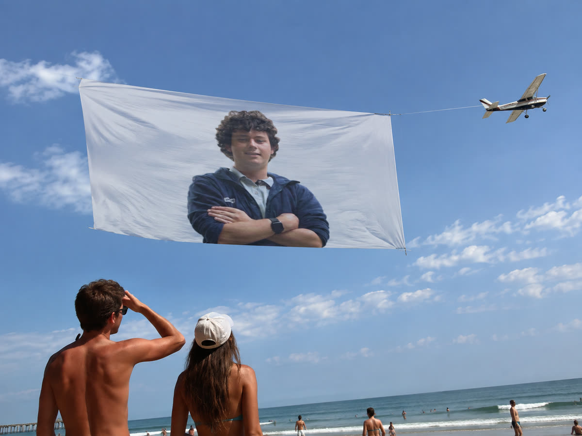 An aerial banner of Chris Ilic towed by a light aircraft over a beach